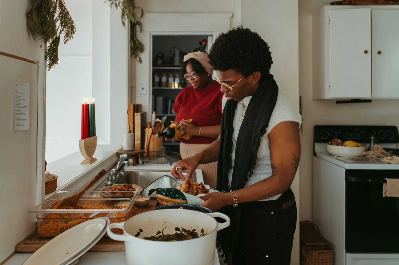 Two people plating home-cooked food from serving dishes and a large pot on a kitchen counter